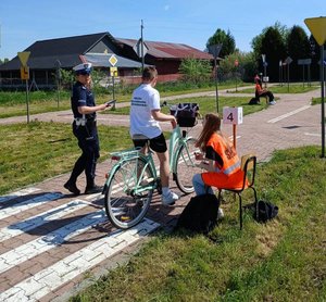 policjantka stoi obok ucznia który jedzie rowerem po miasteczku rowerowym