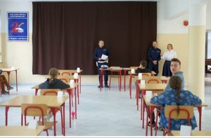 uczniowie siedzą w klasie rozwiązują testy przed nimi stoją policjanci