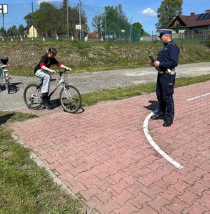 policjant obserwuje przejazd ucznia rowerem po miasteczku rowerowym