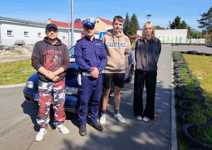 policjant stoi w towarzystwie młodzieży za nimi stoi samochód