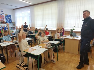 policjant prowadzi w klasie spotkanie z uczniami siedzącymi w ławkach