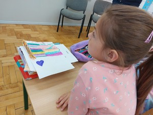 dziewczynka siedzi przy ławce na której leży laurka dla policjanta
