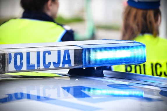 Belka policyjnego radiowozu z napisem policja, w tle postać policjanta