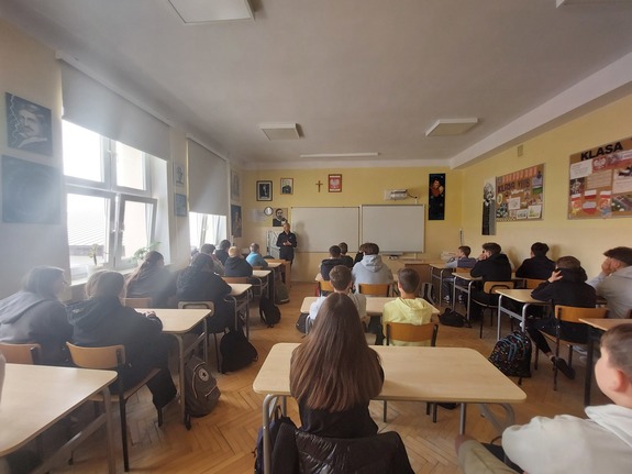 policjantka podczas prelekcji dla uczniów w klasie. Uczniowie siedzą w ławkach przed nimi stoi policjantka