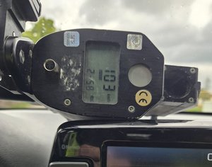 policyjne urządzenie do pomiaru prędkości pojazdów leży na desce rozdzielczej pojazdu z wyświetloną wartością 103 km/h