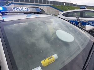 policyjny radiowóz za szybą czołową leży policyjna czapka ruchu drogowego oraz urządzenie do badania stanu trzeźwości