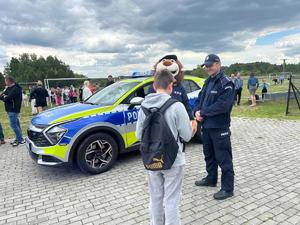 radiowóz obok którego stoi policjant oraz policyjna maskotka lew