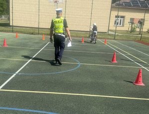 policjant ruchu drogowego idzie za dzieckiem jadącym rowerem po miasteczku rowerowym