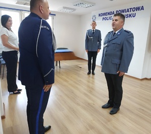 policjanci stoją naprzeciw siebie jeden drugiemu składa meldunek w sali narad