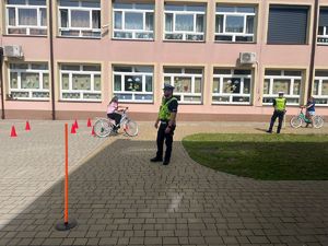 policjanci podczas prowadzenia egzaminu na kartę rowerową dzieci jeżdżą na rowerach na placu przed szkołą