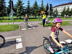 policjant prowadzi egzamin na kartę rowerową dzieci jada na rowerach przez miasteczko ruchu drogowego w tle budynek szkoły