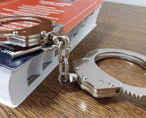 na blacie stolika leży kodeks karny, na kodeksie karnym leżą kajdanki