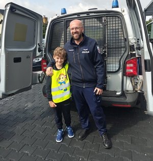 dzieci podczas oglądania policyjnego radiowozu przy budynku policji dziecko stoi z policjantem na tle radiowozu