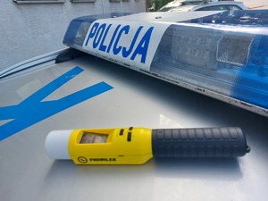 urządzenie do badania stanu trzeźwości leży na dachu radiowozu policyjnego obok belki policyjnej z napisem policja