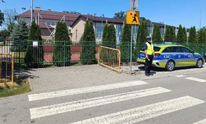 policjant stoi przy radiowozie koło przejścia dla pieszych przed szkołą