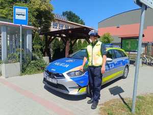 policjant stoi przy radiowozie obok przystanku autobusowego przed szkołą