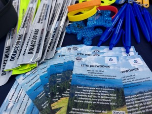 ulotki informacyjne na temat konkursu letni przewodnik oraz długopisy i elementy odblaskowe na stoisku profilaktycznym