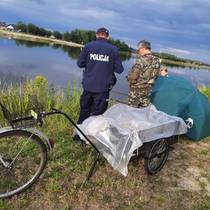policjant stoi nad woda obok wędkarza