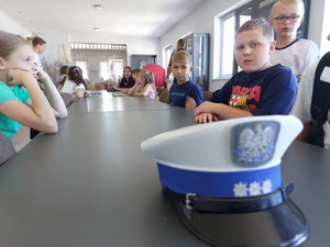 dzieci siedzą przy stole na którym leży policyjna czapka