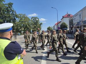 wojsko podczas przemarszu przez ulicę w tle policjant obserwujący przejście