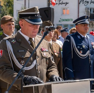 wojskowi oraz policjant stoją w rzędzie jeden z wojskowych przemawia z mównicy