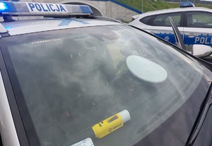 za szybą policyjnego radiowozu leży urządzenie do badania stanu trzeźwości oraz policyjna czapka