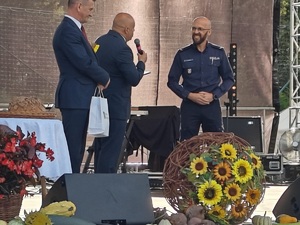 policjant stoi na scenie obok niego dwóch mężczyzn wręcza mu statuetkę