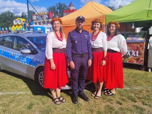 policjant stoi przy radiowozie z uczestnikami dożynek