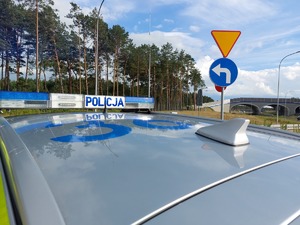 policyjny radiowóz przy drodze obok znak ustąpienia pierwszeństwa i nakaz skrętu w tle wiadukt