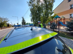 policyjny radiowóz obok budynku szkoły na poboczu stoi policjant