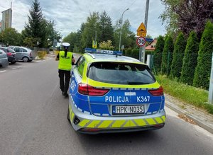policyjny radiowóz obok budynku szkoły obok stoi policjantka