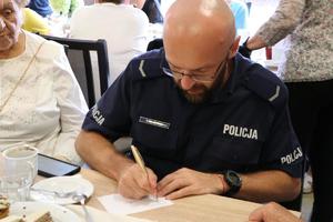 policjant wypełnia karteczki siedząc przy seniorze