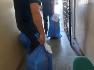 policjanci wynoszą niebieskie wypełnione worki foliowe przez korytarz