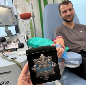 mężczyzna leży na fotelu medycznym do ręki ma podpięte medyczne wenflony w tle osoba trzyma policyjną odznakę z napisem policja 
Zdjęcie wykonania Krzysztof Luchowski