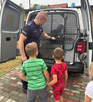 policjant pokazuje dwóm chłopcom policyjny radiowóz