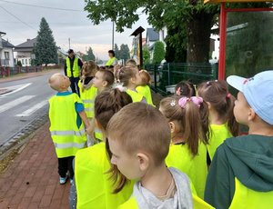 dzieci z policjantem stoją na chodniku w pobliżu przejścia dla pieszych