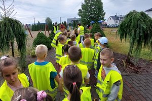 dzieci idą wzdłuż chodnika w kamizelkach odblaskowych