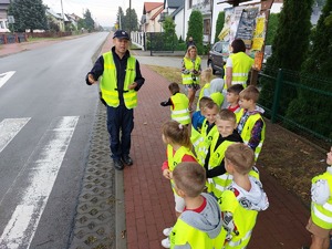 policjant z dziećmi podczas przejścia przez przejście dla pieszych dzieci ubrane są w kamizelki odblaskowe