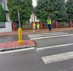 dzieci z policjantem stoją na chodniku przed jezdną