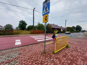 policjanty z dziećmi przy przejściu dla pieszych w tle znaki drogowe