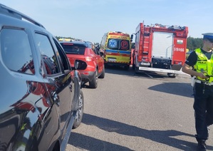 miejsce zdarzenia drogowego karetka pojazdy cywilne i wóz strażacki w tle policjant