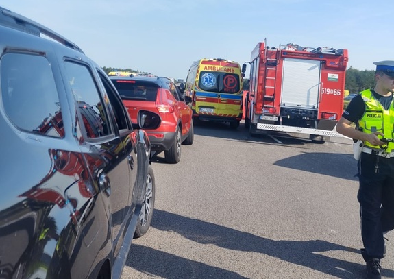 miejsce zdarzenia drogowego karetka pojazdy cywilne i wóz strażacki w tle policjant