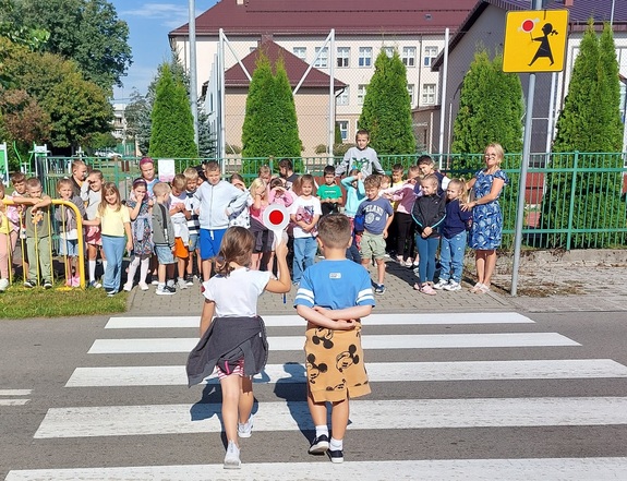 grupa dzieci stoi na chodniku dwoje dzieci idzie w ich stronę przez przejście dla pieszych