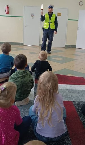 Policjant pokazuje dzieciom latarkę policyjną.