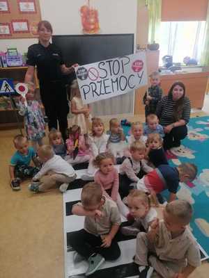 Policjantka stoi, a dzieci siedzą i trzymają baner na którym jest napisane:&quot;Stop przemocy&quot;.