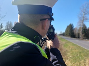 Policjant trzyma urządzenie do pomiaru prędkości i patrzy przez wizjer.