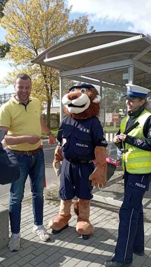 Policjantka ruchu drogowego wręcza mężczyźnie opaskę odblaskową.
