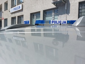 belka świetlno-dźwiękowa na dachu szarego radiowozu na tle budynku komendy.