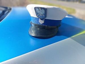 biała czapka policjanta ruchu drogowego lezy na pokrywie silnika radiowozu.