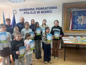 Laureaci konkursu Bezpieczne Wakacje 2025 z Komendantem Powiatowym Policji w Nisku i dwiema policjantkami na tle napisu Komenda Powiatowa Policji w Nisku.